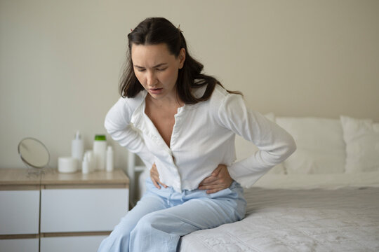 Woman suffering from menstrual pain and abdominal cramps while sitting on a bed at home