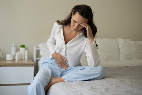 Woman suffering from menstrual pain and abdominal cramps while sitting on a bed at home