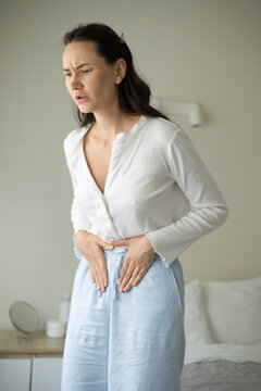 Woman suffering from menstrual pain and abdominal cramps while sitting on a bed at home