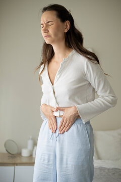 Woman suffering from menstrual pain and abdominal cramps while sitting on a bed at home