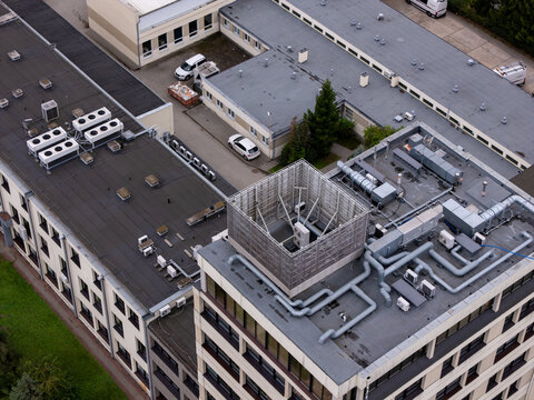 Aerial view of industrial building rooftops featuring multiple HVAC units, ventilation pipes, and a central metal enclosure in Gdansk, Poland.