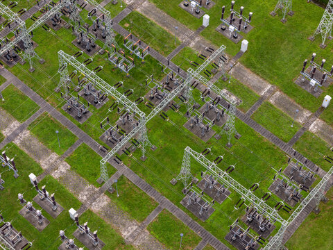 Aerial view of an electrical substation featuring high-voltage power lines, metal towers, and transformers set within a green grassy field in Gdansk, Poland.