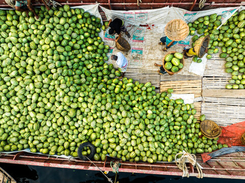 Aerial view of workers loading and unloading a large shipment of watermelons onto a wooden boat at Sadarghat in Dhaka, Dhaka Division, Bangladesh.