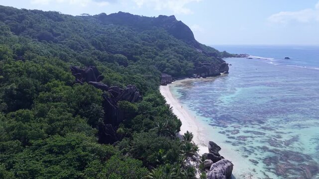Aerial view of Anse Reunion beach with lush tropical forest, granite boulders, and turquoise water in Anse Reunion, La Digue, Seychelles.