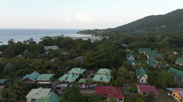 Aerial view of Anse Reunion with houses featuring green roofs nestled in lush tropical vegetation along the coast of Anse Reunion, La Digue, Seychelles.