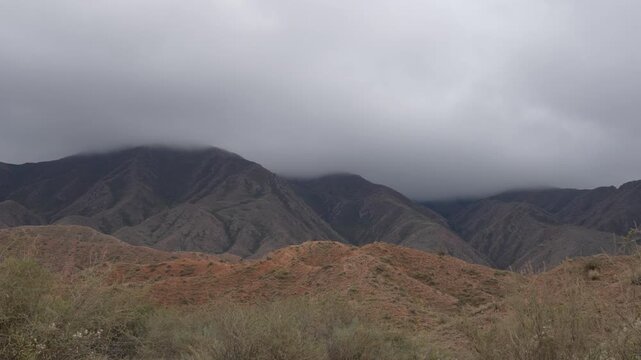 4K panning shot from right to left of dramatic mountain ranges under low thick clouds on the way to Skazka Canyon Kyrgyzstan