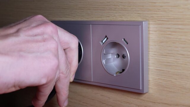 4K close up footage of hand plugging black power cord plug into modern wall outlet socket