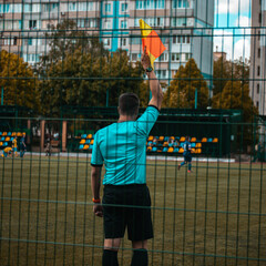 Soccer referee raising assistant flag on sports field during football match behind fence. © Павел Приходько