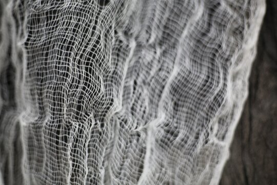 A close-up view showing the detailed grid texture of white gauze or cheesecloth material against a dark background.   