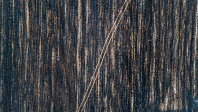 Aerial view of a freshly plowed agricultural field with distinct soil textures and parallel tractor tracks in Sremska Mitrovica, Vojvodina, Serbia.