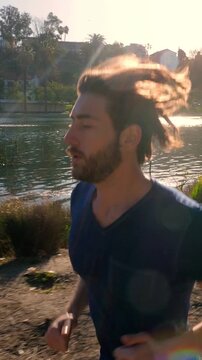 Athletic man jogs around a small lake in Los Angeles. Vertical video.