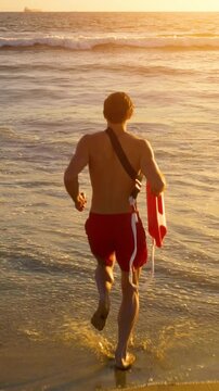 Male lifeguard running along the beach. Vertical video.