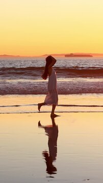 Attractive Asian woman enjoys a walk on the beach at sunset in Southern California. Slow Motion. Vertical Video.