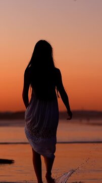 Attractive Asian woman enjoys a walk on the beach at sunset in Southern California. Slow Motion. Vertical Video.