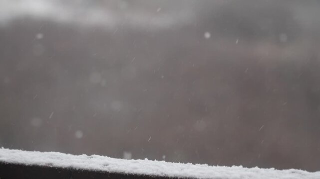 A thin white layer builds on an outdoor surface as soft flakes cross the shallow focus background. The scene supports snowfall measurement, cold alerts, property care and seasonal details.