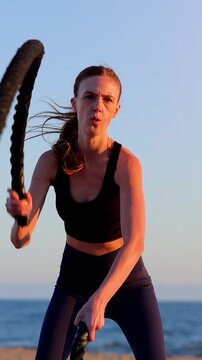 Attractive woman working out on the beach with battle ropes at sunset. Slow Motion. Vertical video.