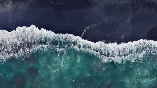 Aerial looking down at waves on a black sand beach in Bali Indonesia.