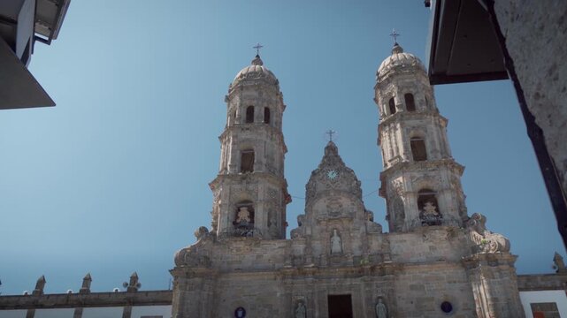 Basilica of Our Lady of Zapopan facade featuring colonial architecture, twin towers, central entrance, surrounding white walls with windows, and visitors walking under clear blue sky