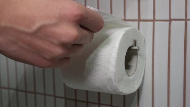 4K close up footage of hand pulling and unrolling white soft toilet paper from metal holder in bathroom