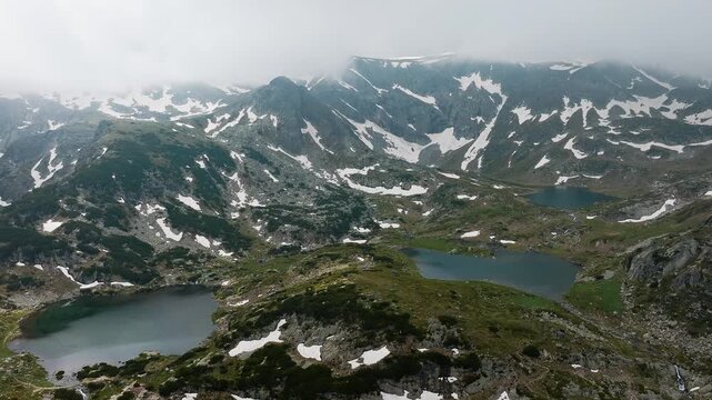 Seven Rila Lakes national park aerial drone view mountain range mist fog summer snow patches glacial lakes Bulgaria hiking hiking trail altitude nature reserve panoramic landscape high angle