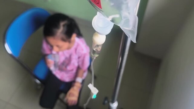 a little girl sitting on a chair with a tube and IV stand attached to her right hand