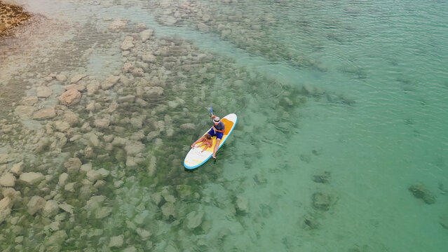 Horizontal aerial top down view of father and little daughter paddleboarding on stand up paddle board in turquoise clear water of Kournas lake in Crete Greece