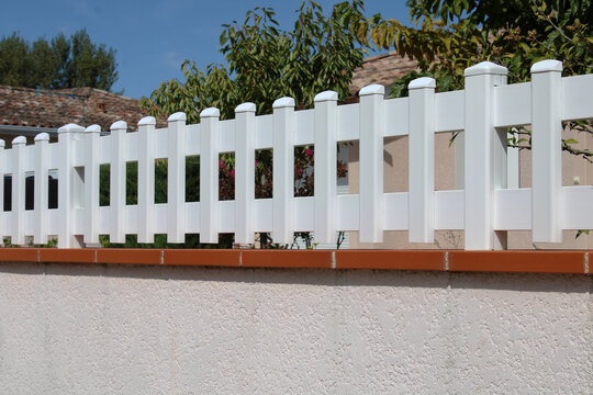 Cl&ocirc;ture de jardin en PVC blanc avec chapeaux bomb&eacute;s sur muret en briques et cr&eacute;pi