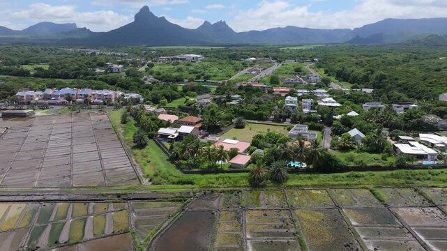 Aerial view of Salines de Yemen-Tamarin salt pans with surrounding residential houses and lush greenery against a backdrop of mountains in Tamarin, Riviere Noire District, Mauritius.