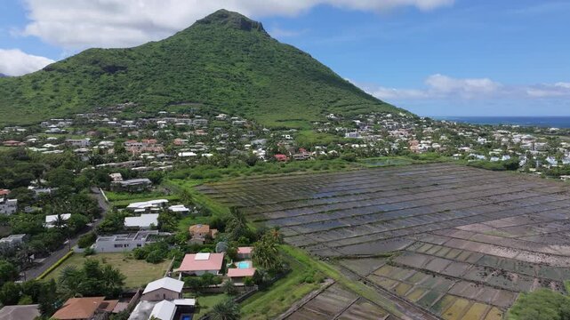 Aerial view of Salines de Yemen-Tamarin salt pans with surrounding residential area and lush green mountain in Tamarin, Riviere Noire District, Mauritius.