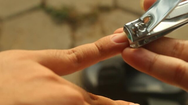 Close-up of a hand trimming fingernails with a stainless steel nail clipper, illustrating personal grooming, nail care, hygiene, self-care, and everyday hand care.