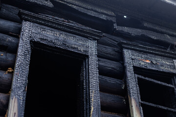 Charred wooden cabin window exterior with burnt log siding and cracked frame for fire damage © Parilov