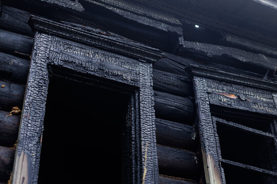 Charred wooden cabin window exterior with burnt log siding and cracked frame for fire damage