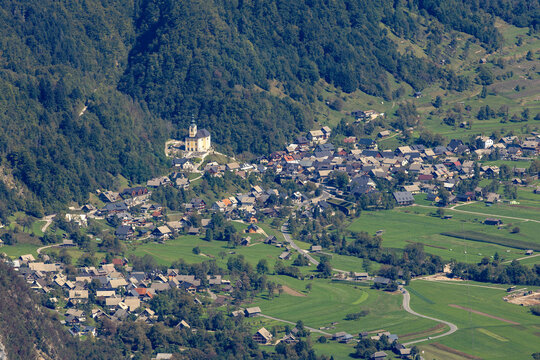 Aerial view of the village of Srednja Vas v Bohinju featuring its prominent church, traditional houses, and surrounding green meadows in Srednja Vas v Bohinju, Slovenia.