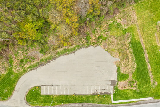 Top down aerial view of a small paved parking lot nestled in a wooded area with paved space asphalt surface grassy field outdoor site marked spaces nature surroundings land development