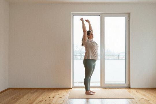 Plus-size woman stretching on a yoga mat by a window