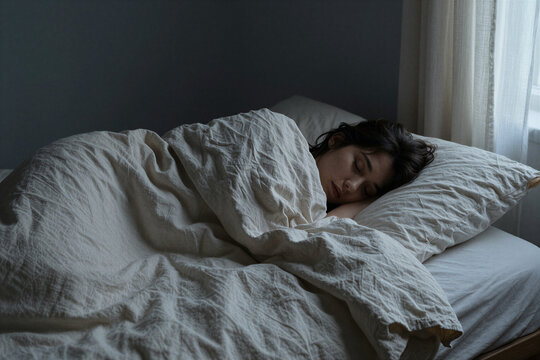 Woman sleeping peacefully under a linen duvet at dawn