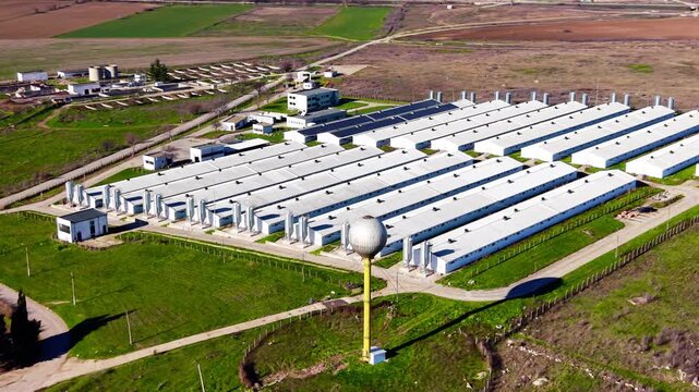 Aerial view of large poultry farm complex, Bulgaria. Overhead drone perspective reveals rows of barn roofs, silos, solar panels and green fields.