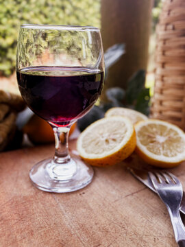 Red wine glass standing next to sliced lemons, a knife, and a fork on a worn wooden board, suggesting a gourmet outdoor meal, barbecue, or an Argentinian asado celebration