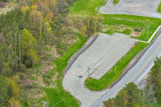 Aerial view of a paved parking lot turn around area surrounded by lush green trees and natural forest landscape with paved surface drone photography outdoor space land use landscape greenery