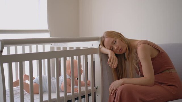 Burnt-out mother looking at crying baby in crib. Video with natural sound.