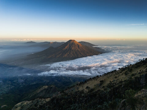 Aerial view of Gunung Sumbing rising above a sea of clouds during golden hour in Kecamatan Kalikajar, Jawa Tengah, Indonesia.