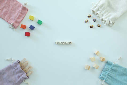 PROJECT spelled with letter tiles among colorful craft materials and pastel fabric bags on a bright flat lay with generous copy space.