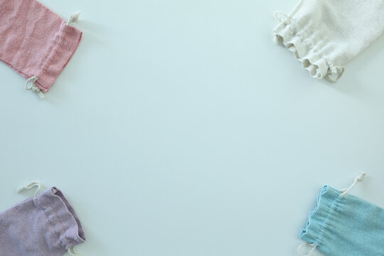 Four pastel fabric drawstring bags arranged around a bright blank background with generous central copy space for text or design.