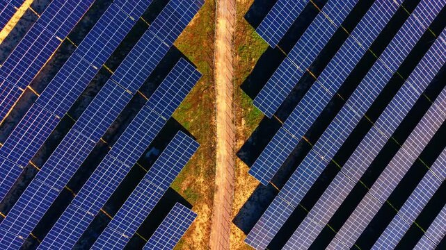Overhead pattern of converging solar panel rows, Bulgaria. Drone view captures zigzag panel edges, dirt trail and scattered green patches.