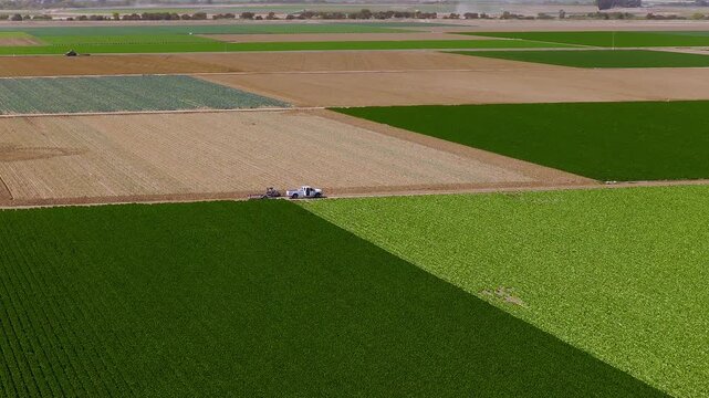 Aerial view reveals geometric crop fields and dirt farm roads in California with a white pickup truck parked beside planted rows under bright sunshine.