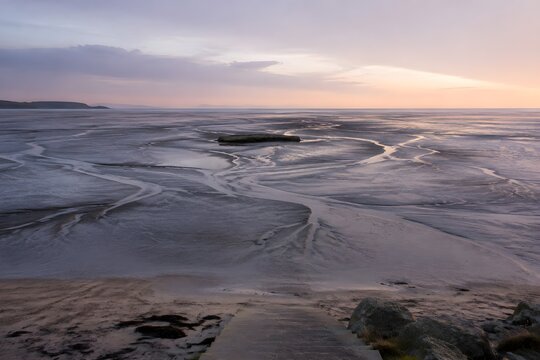 Vast damp tidal flat at low water with shallow braided channels and lone flat rock outcrop