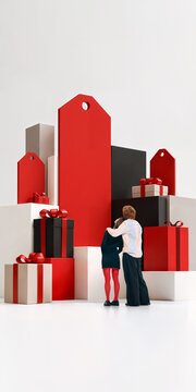 Young couple embrace beside oversized gifts and giant price tags with warm excitement. Gift shopping, seasonal offers, loyalty rewards concept.