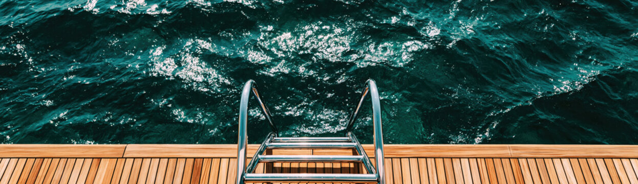 Top view of polished wooden boat deck beside dark ocean water and metal boarding ladder creating calm maritime scene