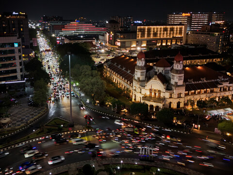 Aerial view of the illuminated historic Lawang Sewu building at night with busy traffic light trails on the surrounding streets in Semarang, Central Java, Indonesia.