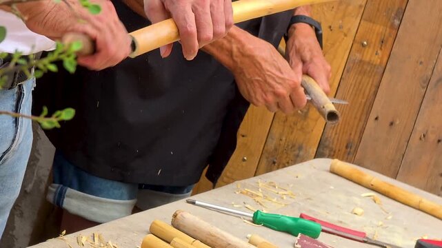 Close up of artisan hands carving a traditional Spanish dolcaina wind instrument from reed stem, handmade musical instrument craft.
